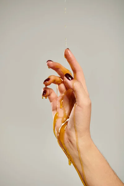 Mani di donna sconosciuta con smalto scuro ricoperto di miele d'oro organico su sfondo grigio — Foto stock