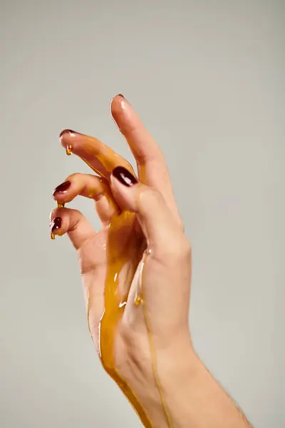 Main de femme inconnue pointant vers le haut tandis que couvert de miel doux doré sur fond gris — Photo de stock