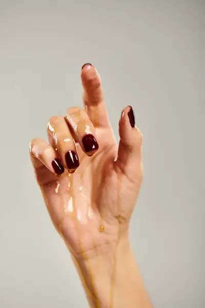 Main de modèle féminin inconnu avec vernis à ongles recouvert de miel doré pur sur fond gris — Photo de stock