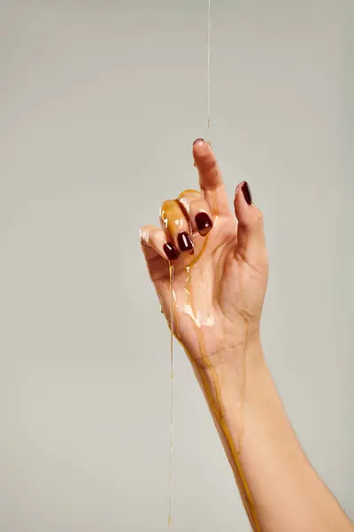 Hand of unknown young female model covered with natural delicious honey on gray background — Stock Photo