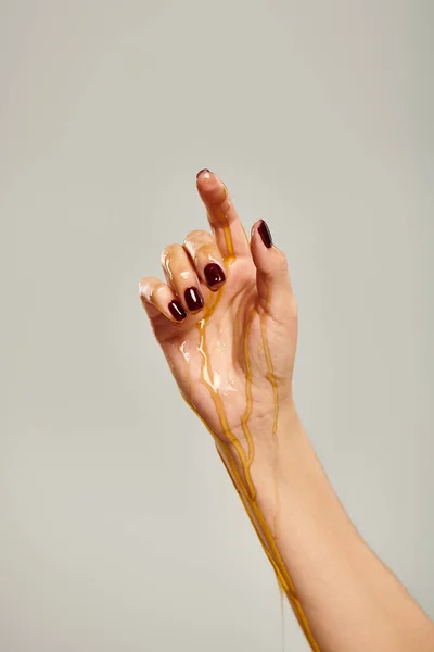 Main de modèle féminin inconnu avec vernis à ongles recouvert de miel délicieux bio sur fond gris — Photo de stock