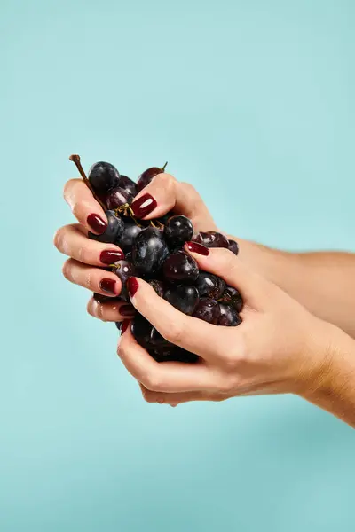 Sconosciuta giovane signora con smalto spremendo uva fresca succosa nelle sue mani su sfondo blu — Foto stock