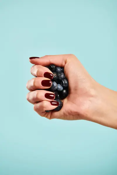 Object photo of fresh juicy blueberries in hand of unknown female model on vibrant blue backdrop — Stock Photo