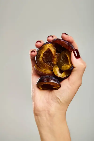 Об'єкт фото свіжих смачних соковитих слив в руці молодої невідомої жінки на сірому фоні — стокове фото