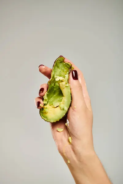 Unknown female model squeezing healthy delicious avocado in her hand while on gray background — Stock Photo