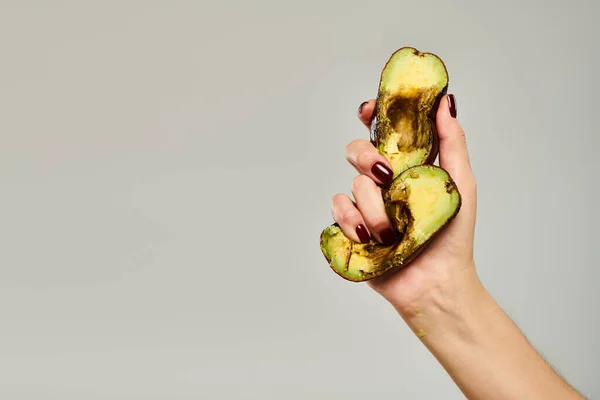 Donna sconosciuta con smalto per unghie spremendo avocado sano gourmet in mano su sfondo grigio — Foto stock