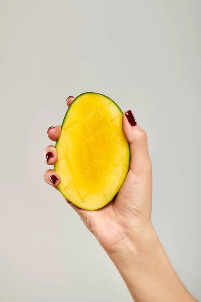 Об'єкт фото гастрономічного соковитого манго в руці молодої невідомої жіночої моделі на сірому фоні — стокове фото