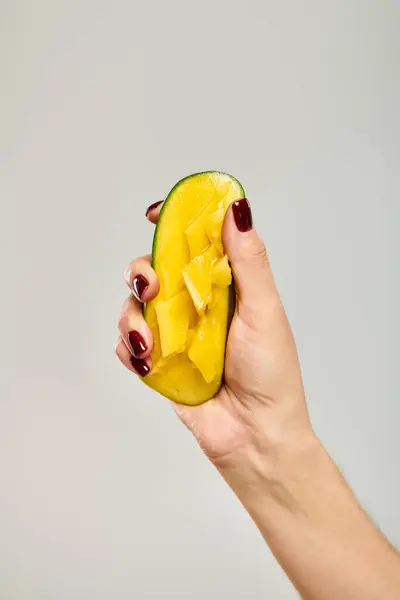 Unknown young female model squeezing juicy sweet mango in her hand while on gray background — Stock Photo