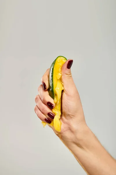 Unknown young female model with nail polish squeezing fresh mango in her hand on gray background — Stock Photo