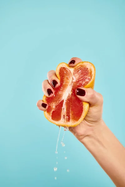 Unknown young female model with nail polish squeezing fresh juicy grapefruit on blue backdrop — Stock Photo