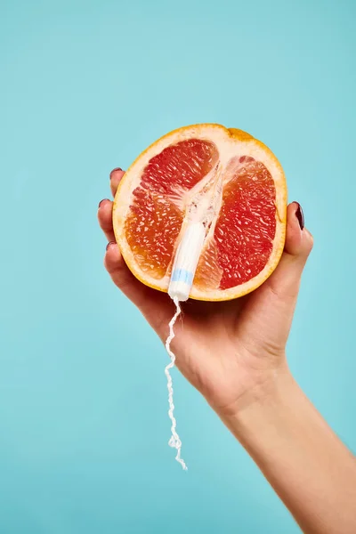 Object photo of fresh juicy grapefruit with tampon in it in hand of unknown woman on blue backdrop — Stock Photo