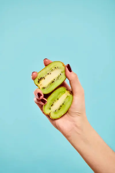 Object photo of delicious green kiwi in hand of unknown female with nail polish on blue backdrop — Stock Photo