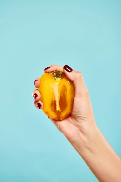Object photo of delicious fresh persimmon in hand of unknown woman with nail polish on blue backdrop — Stock Photo