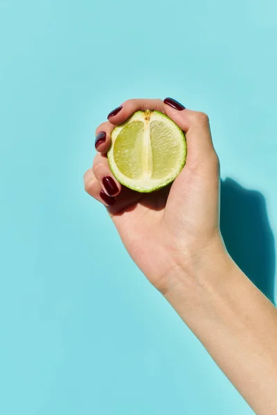 Fresh green lime in hand of unknown young woman with nail polish posing on vibrant blue backdrop — Stock Photo