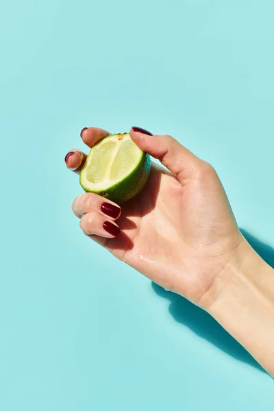 Juicy citrus fresh lime in hand of unknown woman with nail polish posing with it on blue background — Stock Photo