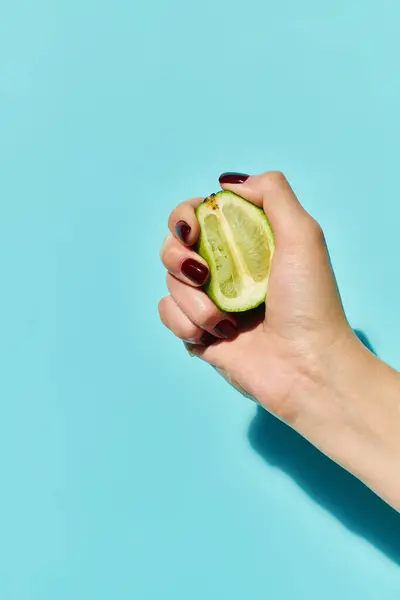 Unknown female model with nail polish squeezing fresh ripe lime in hand on vibrant blue backdrop — Stock Photo
