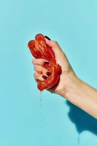 Red juicy delicious pieces of tomato squeezed by unknown female model on vibrant blue background — Stock Photo