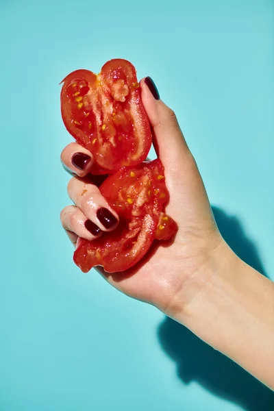 Red delicious gourmet pieces of fresh tomato squeezed by unknown female model on vivid background — Stock Photo