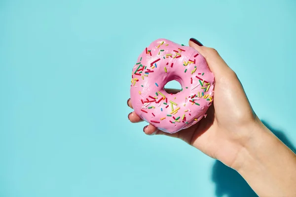 Sweet delicious donut with pink frosting on it in hand of unknown female holding it on pink backdrop — Stock Photo