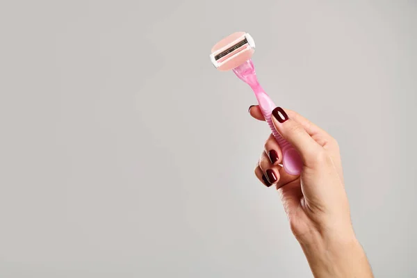 Об'єкт фото рожевої бритви в руці невідомої жіночої моделі з лаком для нігтів на сірому фоні — стокове фото