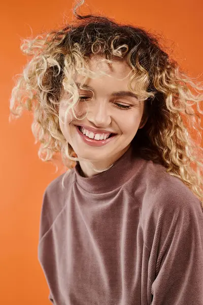 Portrait of charming smiling woman with wavy hair in brown turtleneck on radiant orange background — Stock Photo