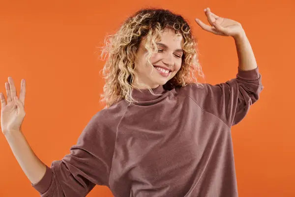 Jolly woman with wavy hair in stylish mocha color turtleneck posing on vibrant orange backdrop — Stock Photo