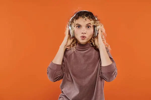 Trendy erstaunt lockige Frau in drahtlosen Kopfhörern Musik hören auf leuchtend orangefarbenem Hintergrund — Stockfoto