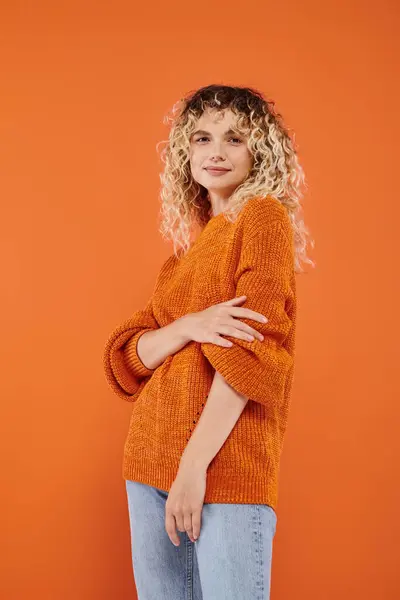 Donna alla moda con i capelli ondulati in accogliente maglione a maglia guardando la fotocamera su sfondo arancione brillante — Foto stock