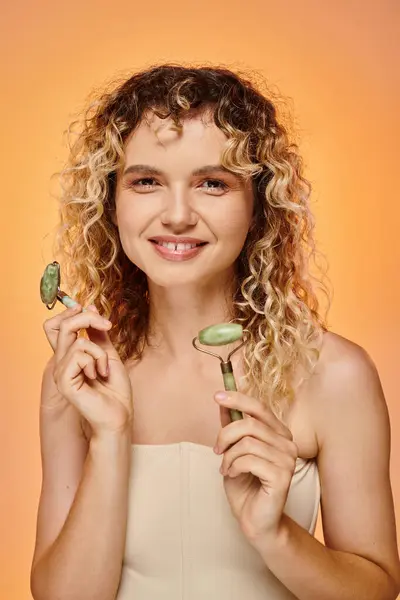 Mulher sorridente com pele perfeita segurando rolos de jade sorrindo para a câmera no fundo gradiente pastel — Fotografia de Stock