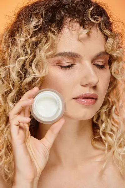 Close up portrait of curly woman with perfect skin showing jar of cosmetic cream in studio — Stock Photo