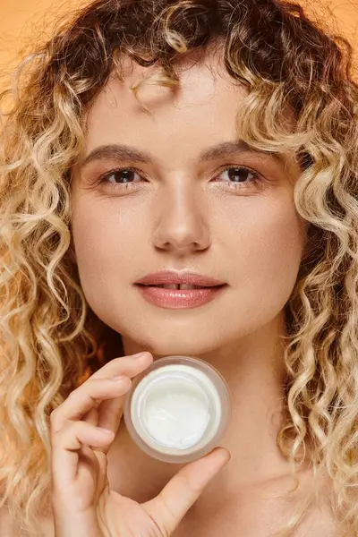 Close up portrait of woman with wavy hair and perfect skin showing face cream on studio backdrop — Stock Photo