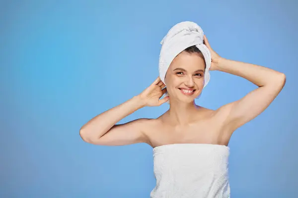 Cheerful woman with perfect skin and towel on head smiling and looking at camera on blue backdrop — Stock Photo