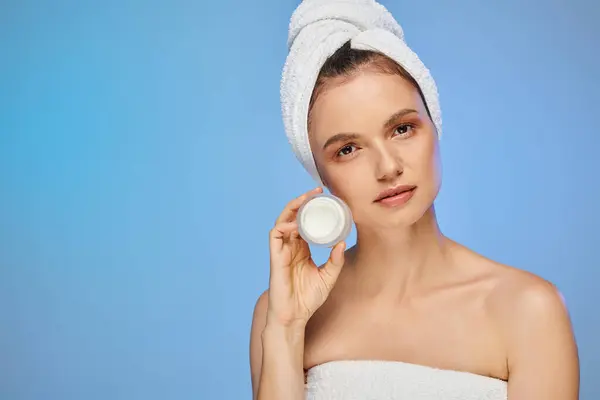 Seductora mujer con toalla en la cabeza mostrando tarro de crema facial sobre fondo azul, bienestar y belleza - foto de stock