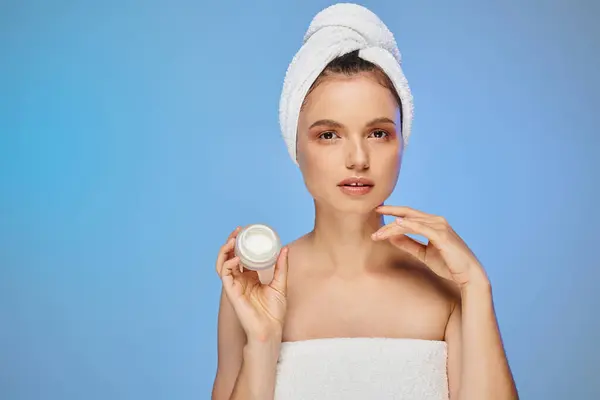 Pretty woman with towel on head showing jar of face cream on blue backdrop, wellness and beauty — Stock Photo
