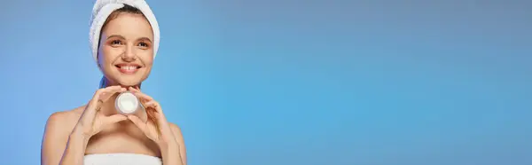 Fröhliche Frau mit Handtuch auf dem Kopf und einem Glas Gesichtscreme auf blauem Hintergrund, horizontales Banner — Stockfoto