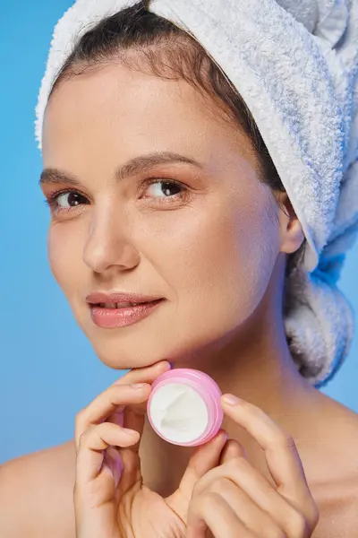 Retrato de mujer sonriente con cara perfecta y toalla en la cabeza con tarro de crema cosmética en azul - foto de stock
