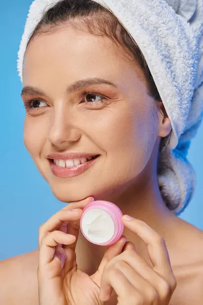Mulher alegre com pele brilhante e frasco segurando toalha de creme cosmético e olhando para o azul — Fotografia de Stock