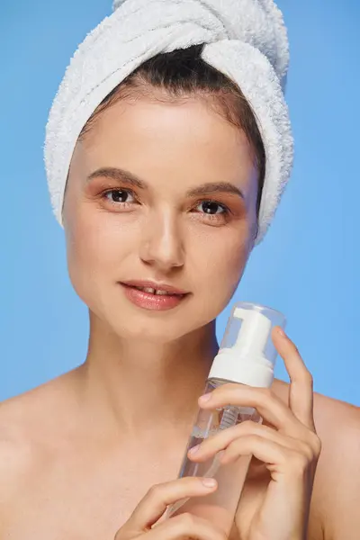 Portrait of woman with towel on head and perfect skin holding dispenser with face foam on blue — Stock Photo