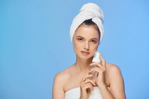 Portrait of model with towel on head and clean skin holding dispenser with face foam on blue — Stock Photo