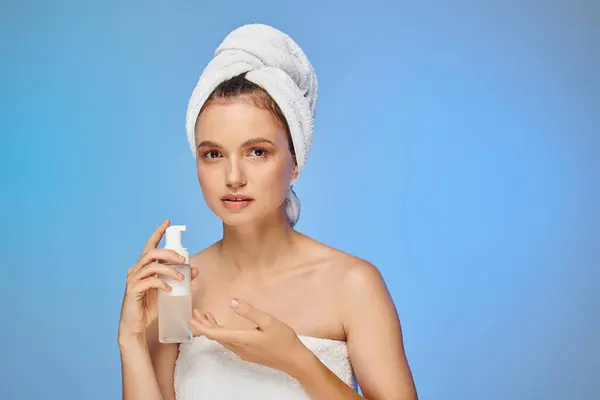 Mulher atraente com toalha na cabeça e rosto perfeito segurando dispensador com espuma cosmética em azul — Fotografia de Stock