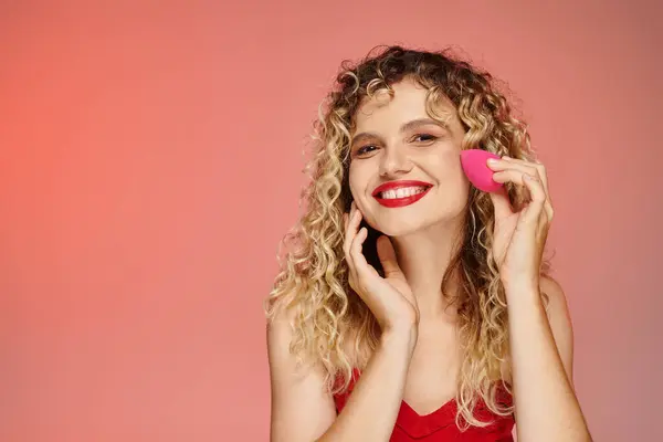 Lockiges, fröhliches Model mit roten Lippen mit Gesichtsschwamm auf rosa und gelben Hintergrund, elegante Schönheit — Stockfoto