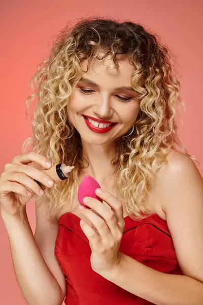 Усміхнена модна жінка наносить макіяж фон на косметичну губку на рожево-жовтий фон — стокове фото