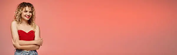 Mujer alegre con labios rojos posando en la parte superior roja y mirando hacia otro lado en rosa y amarillo, bandera - foto de stock