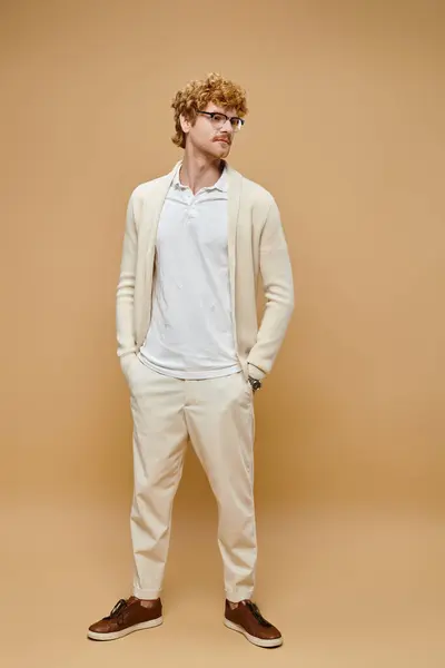 Jeune rousse homme aux lunettes et vieux style argent tenue décontractée avec les mains dans la poche sur beige — Photo de stock