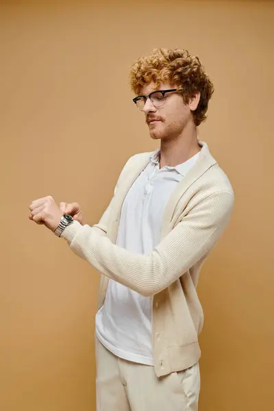 Trendy uomo rossa in occhiali da vista guardando orologio da polso su sfondo beige, senza tempo vecchio denaro moda — Foto stock