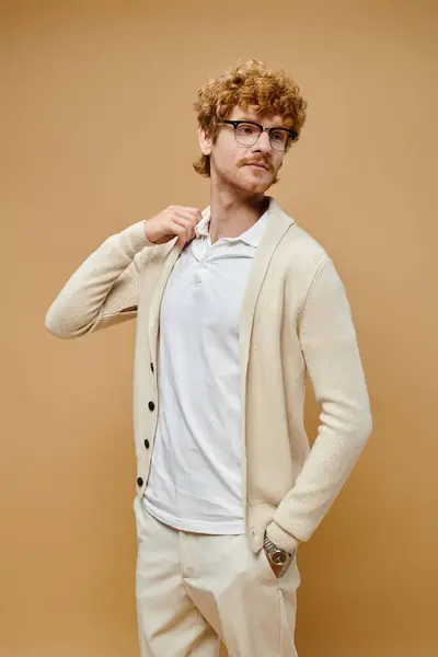 Jeune rousse homme en tenue décontractée à la mode et lunettes regardant loin sur fond beige — Photo de stock