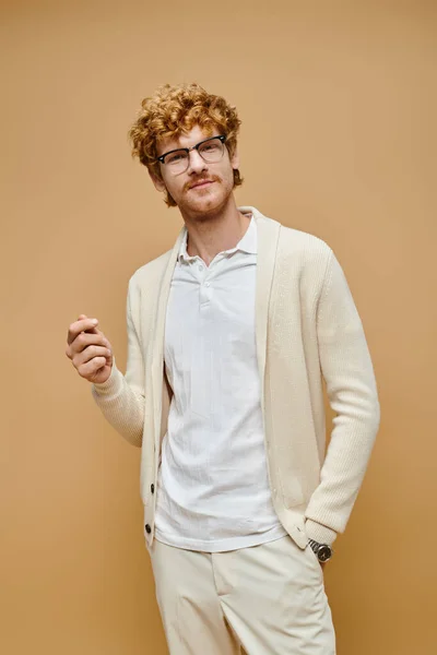 Homme aristocratique dans des lunettes et des vêtements de couleur claire debout avec la main dans la poche sur beige — Photo de stock