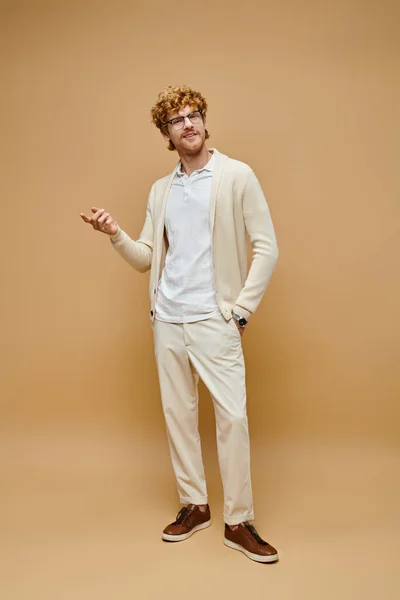 Longueur pleine d'homme rousse élégant en lunettes et vêtements à la mode avec la main dans la poche sur beige — Photo de stock