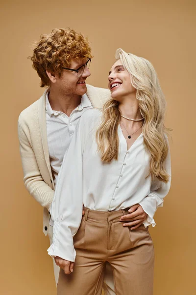 Delighted redhead man and blonde woman in trendy casual attire smiling at each other on beige — Stock Photo