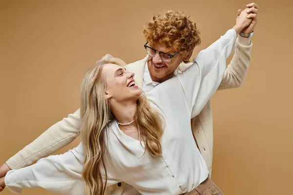 Ravi couple à la mode se tenant la main et se souriant tout en s'amusant sur beige — Photo de stock
